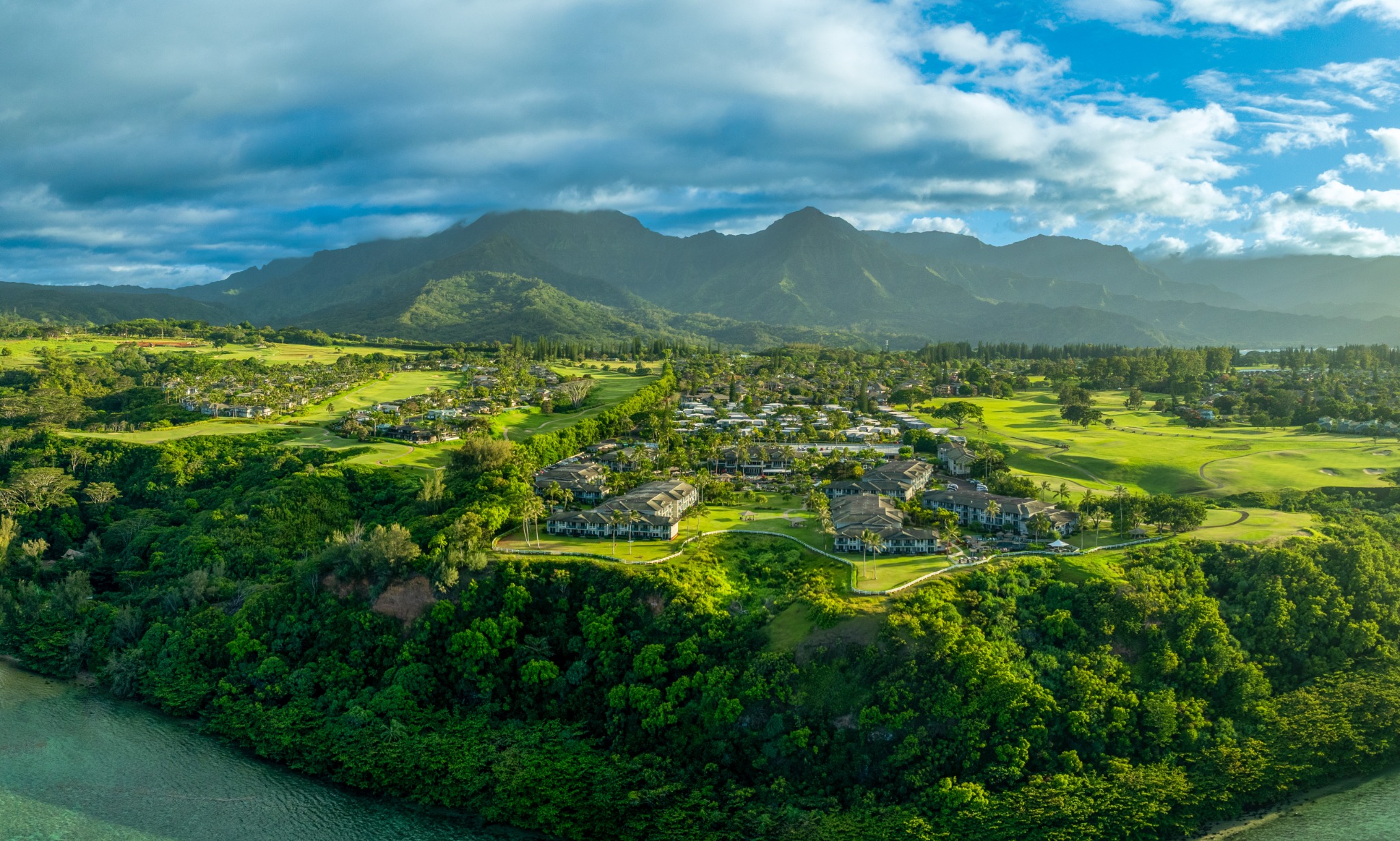 Wide aerial view of Hawaiian coastline, golf course and mountains
